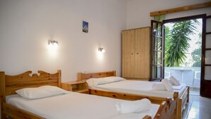 Ein Zimmer mit zwei Holzbetten, einem Holzschrank und einem Fenster mit Blick auf Palmen.