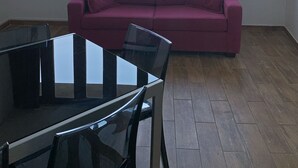Una habitación con un gran ventanal, un sofá morado y una mesa de vidrio.