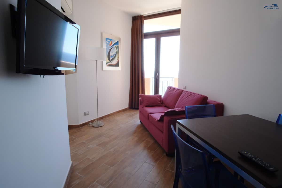 A modern living room with a flat-screen TV, a red sofa, a dining table, and a floor lamp.