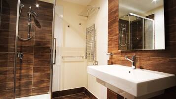 Un baño moderno con ducha de vidrio, lavamanos blanco y un espejo grande.
