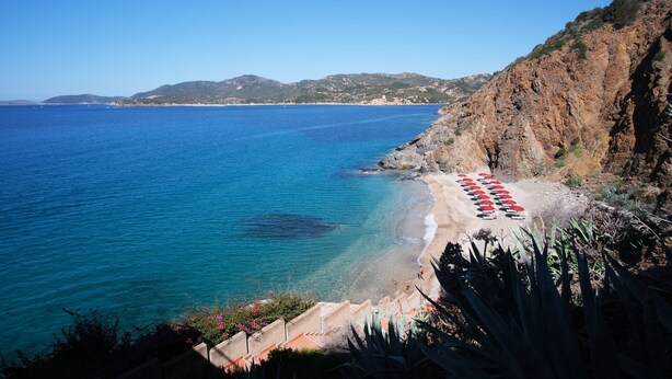 Vista costera con playa, acantilados rocosos y mar azul cristalino.