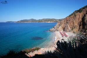 Vista costera con playa, acantilados rocosos y mar azul cristalino.