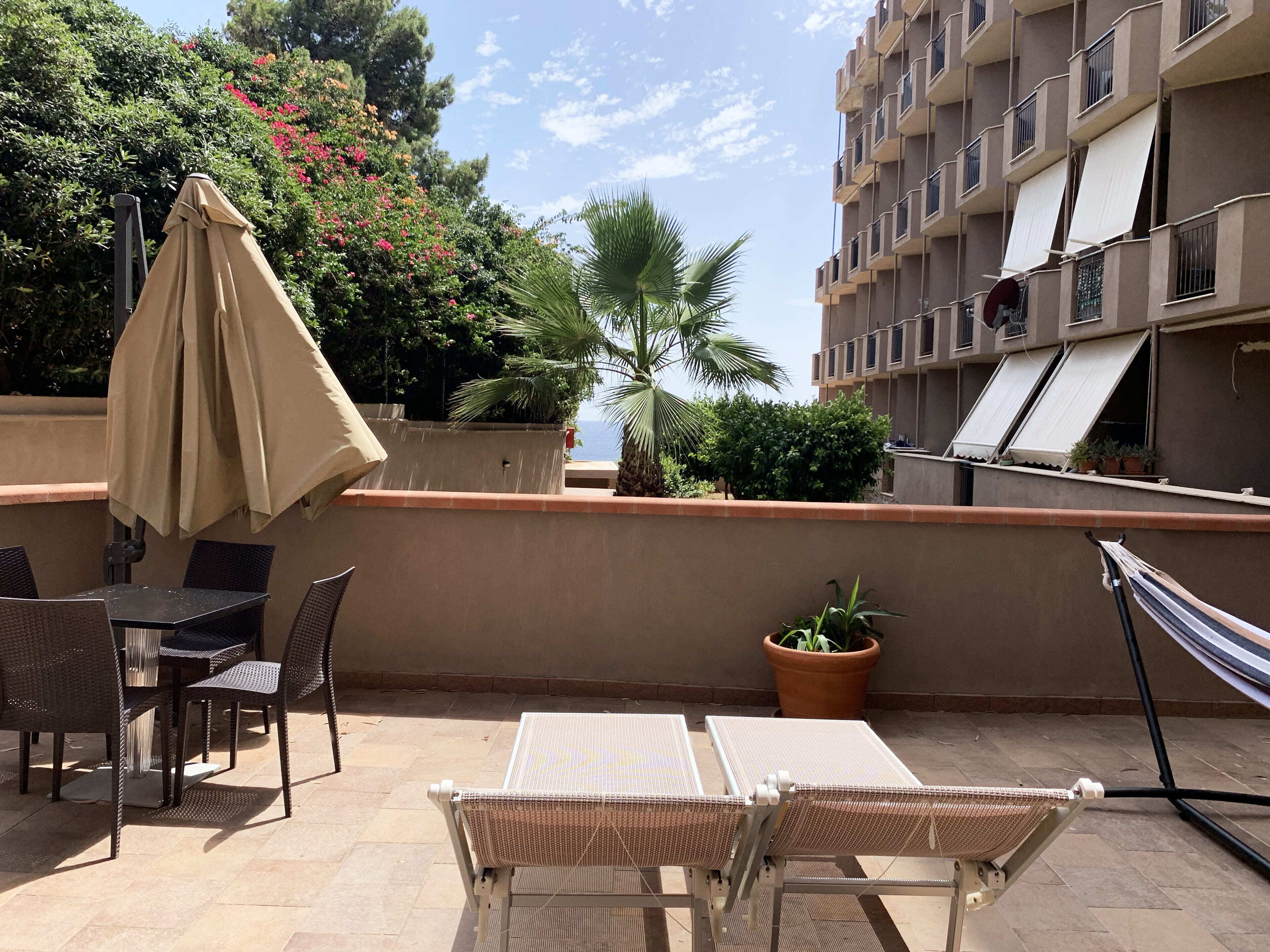 A rooftop terrace with outdoor seating, a hammock, and a view of a building with balconies.