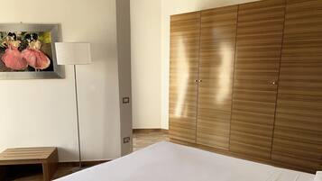Un dormitorio con una cama grande, un armario de madera, un pequeño banco de madera y un cuadro en la pared.