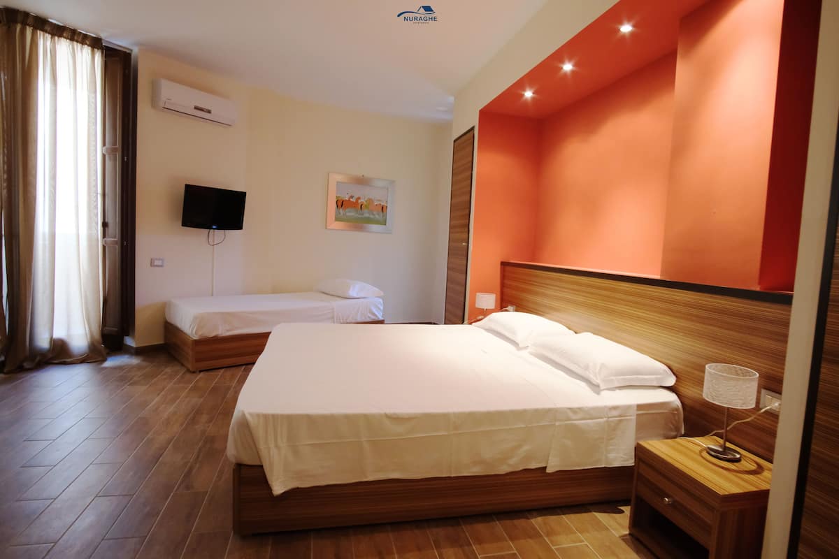 A hotel room with two beds, a television, an air conditioning unit, and a painting on the wall.