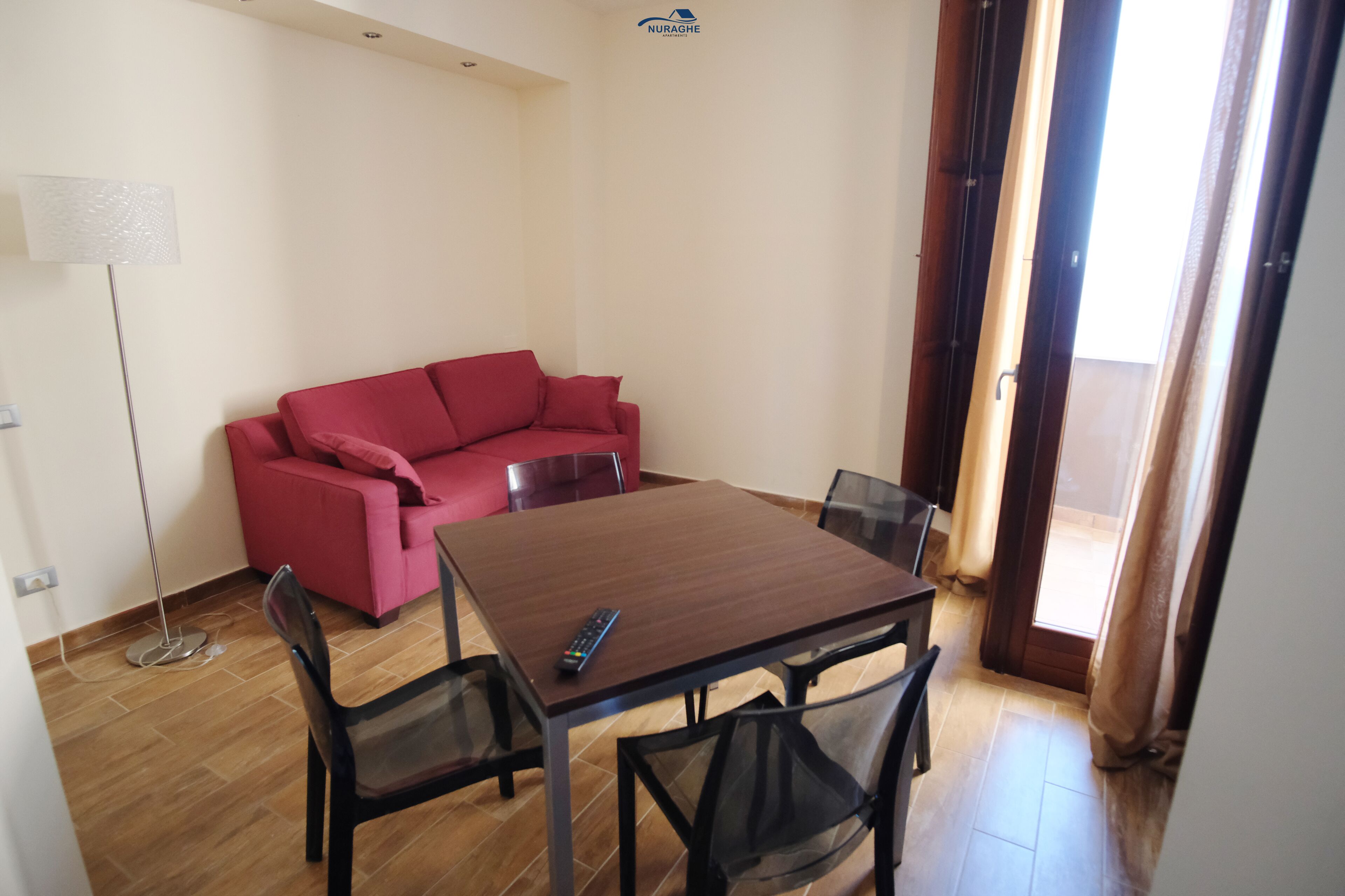 A room with a wooden dining table, four chairs, a red sofa, and a floor lamp.