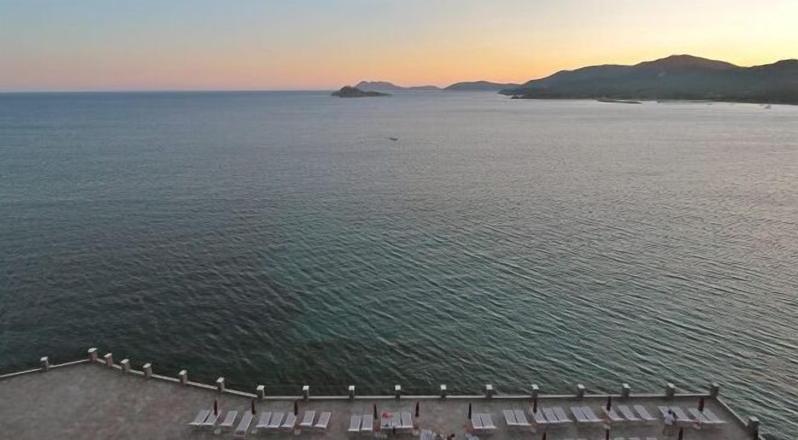 A seaside view with a calm sea, a distant island, and a row of sun loungers along a pier.