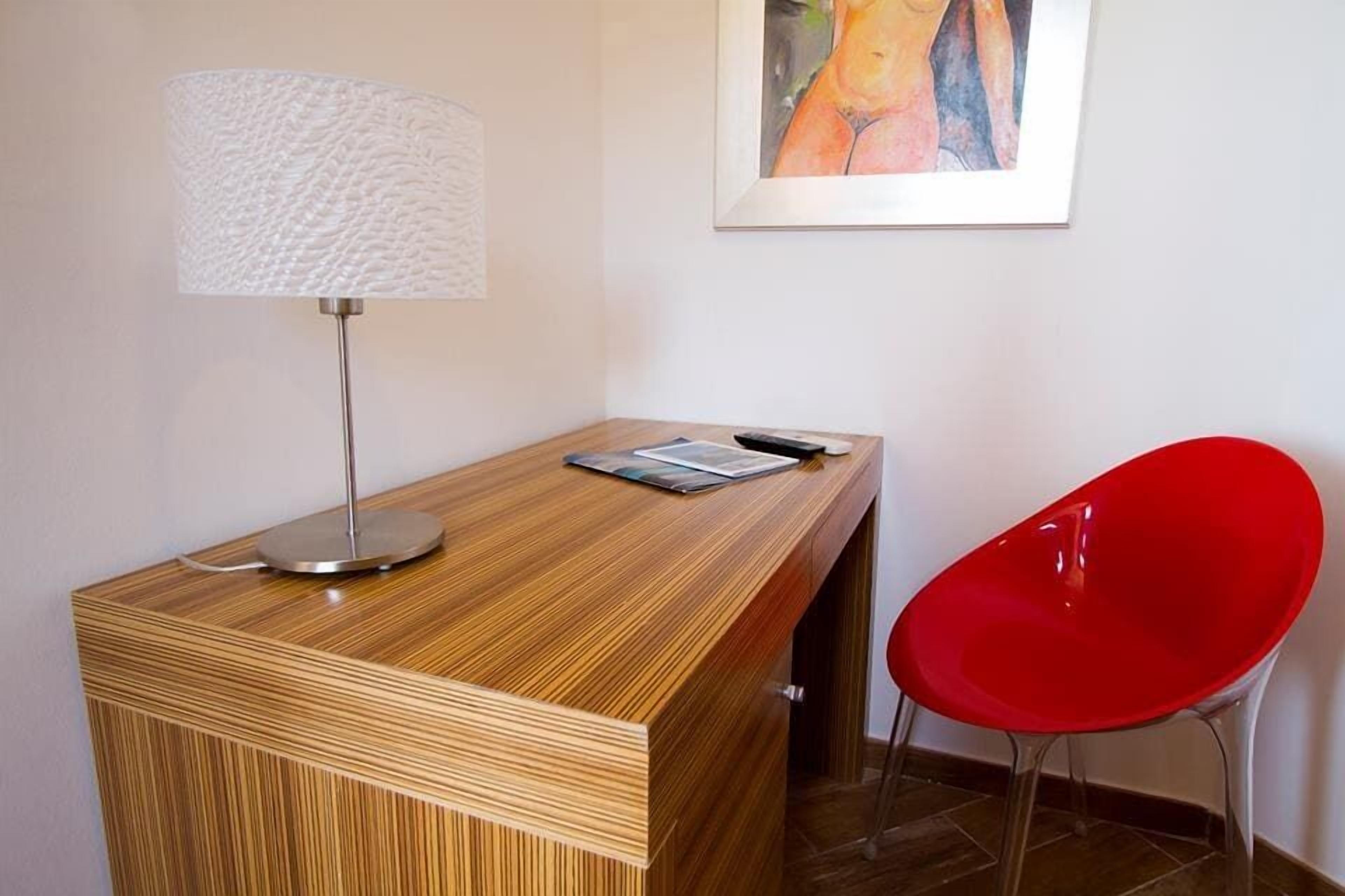 A wooden reception desk with a lamp, a red chair, and a framed painting on the wall.