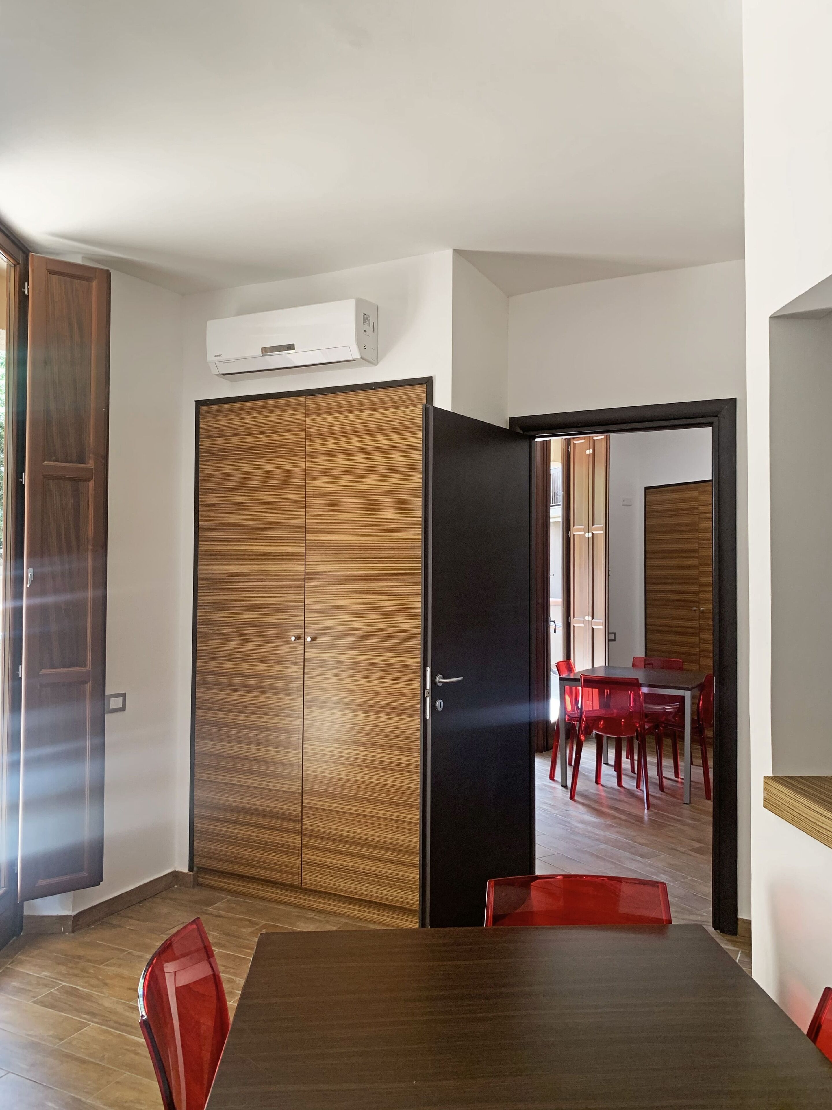 Een moderne kamer met een houten garderobe, een eettafel met rode stoelen en een airconditioning aan de muur.
