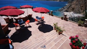 Terraza con sombrillas rojas, mesas al aire libre y plantas en macetas.