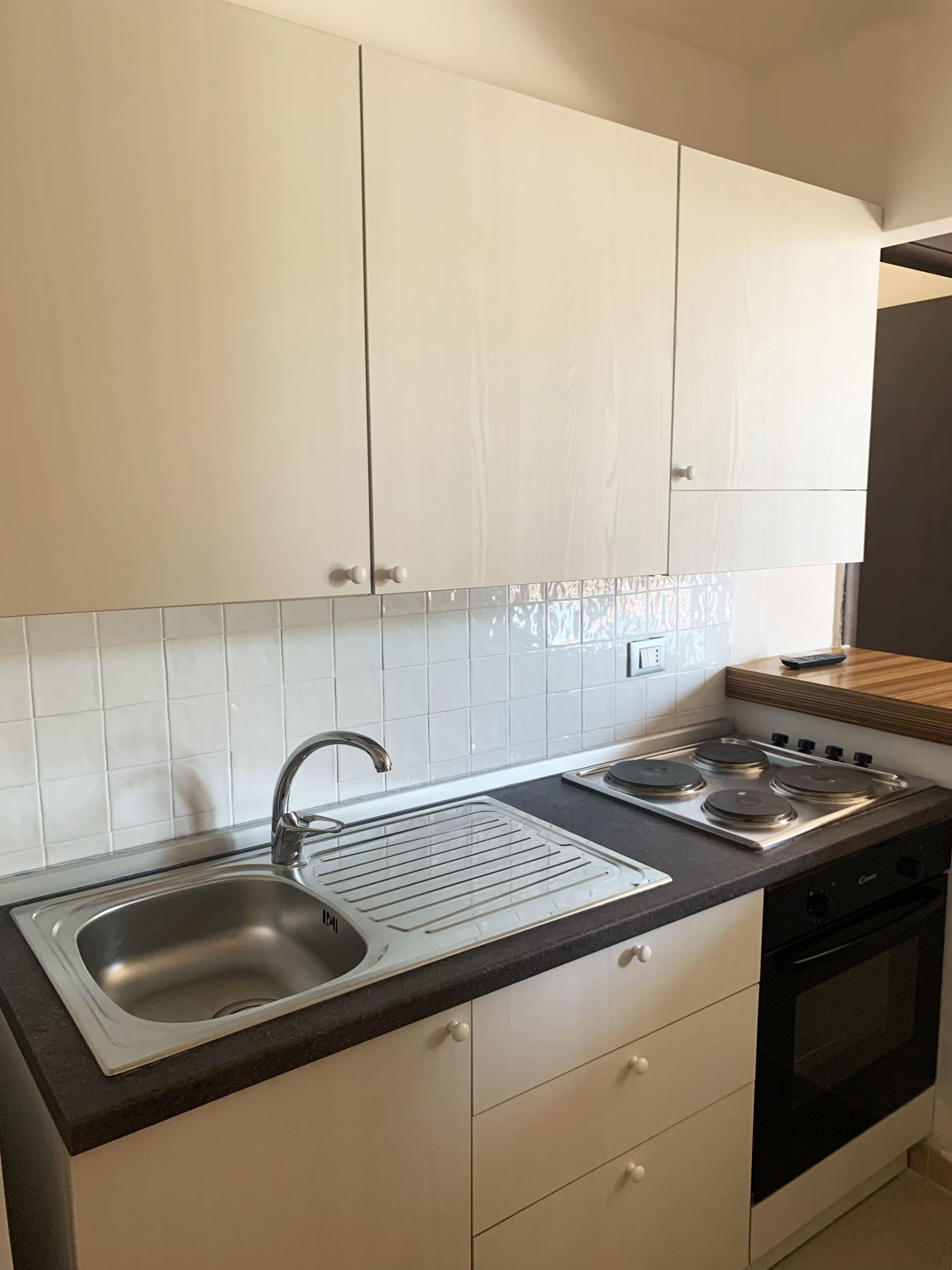 A kitchen with white cabinets, a stainless steel sink, a stove, and a countertop.