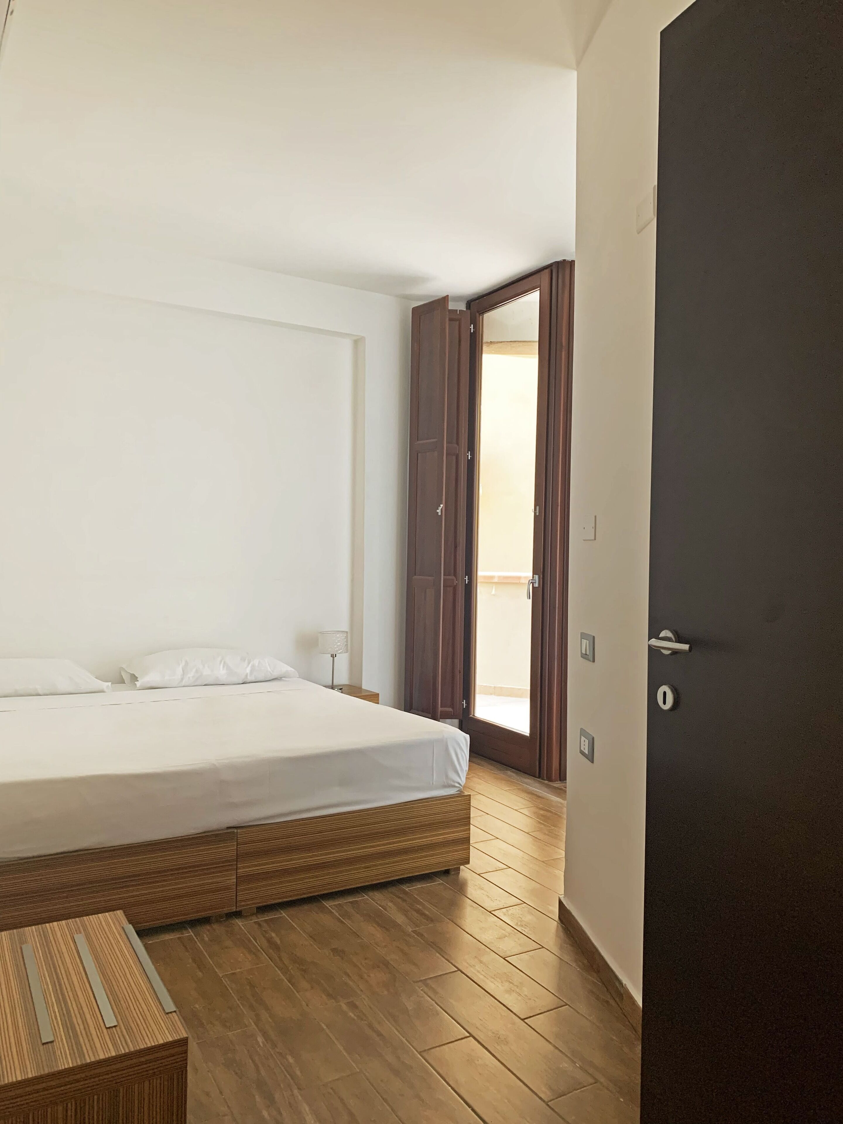 Un dormitorio con cama, piso de madera y puerta que da a un balcón.