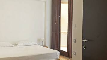Un dormitorio con cama, piso de madera y puerta que da a un balcón.
