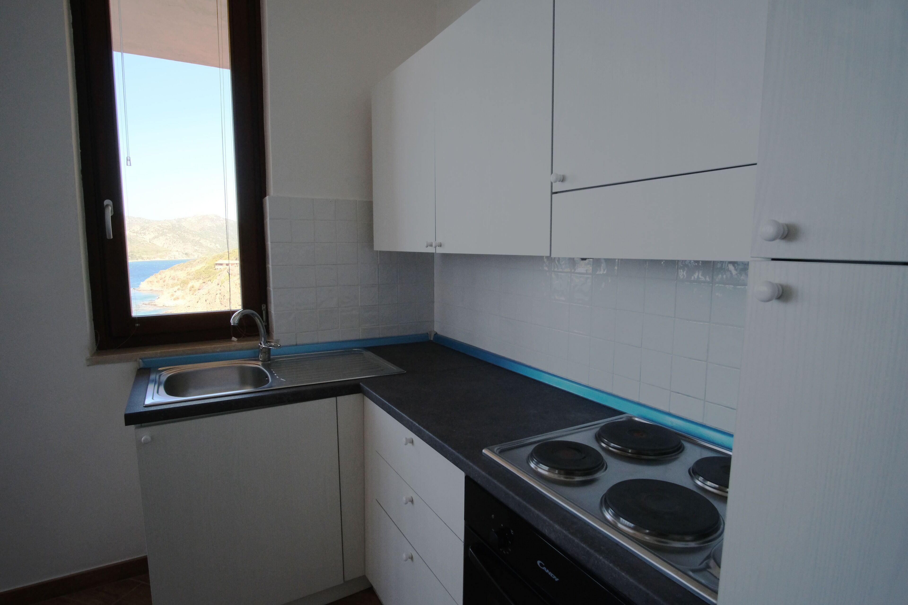 Una cucina con mobili bianchi, un piano di lavoro nero, un lavello e un fornello.