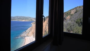Vista costera a través de una ventana con cortinas, mostrando una playa, acantilados y cielo despejado.