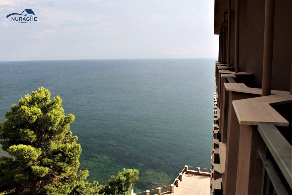 Vista des del balcó sobre el mar, amb cel blau i un edifici de disseny modern.