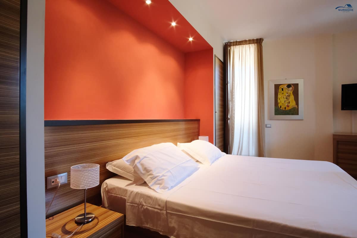 A hotel room with a large bed, a bedside lamp, a painting on the wall, and a television on the opposite wall.