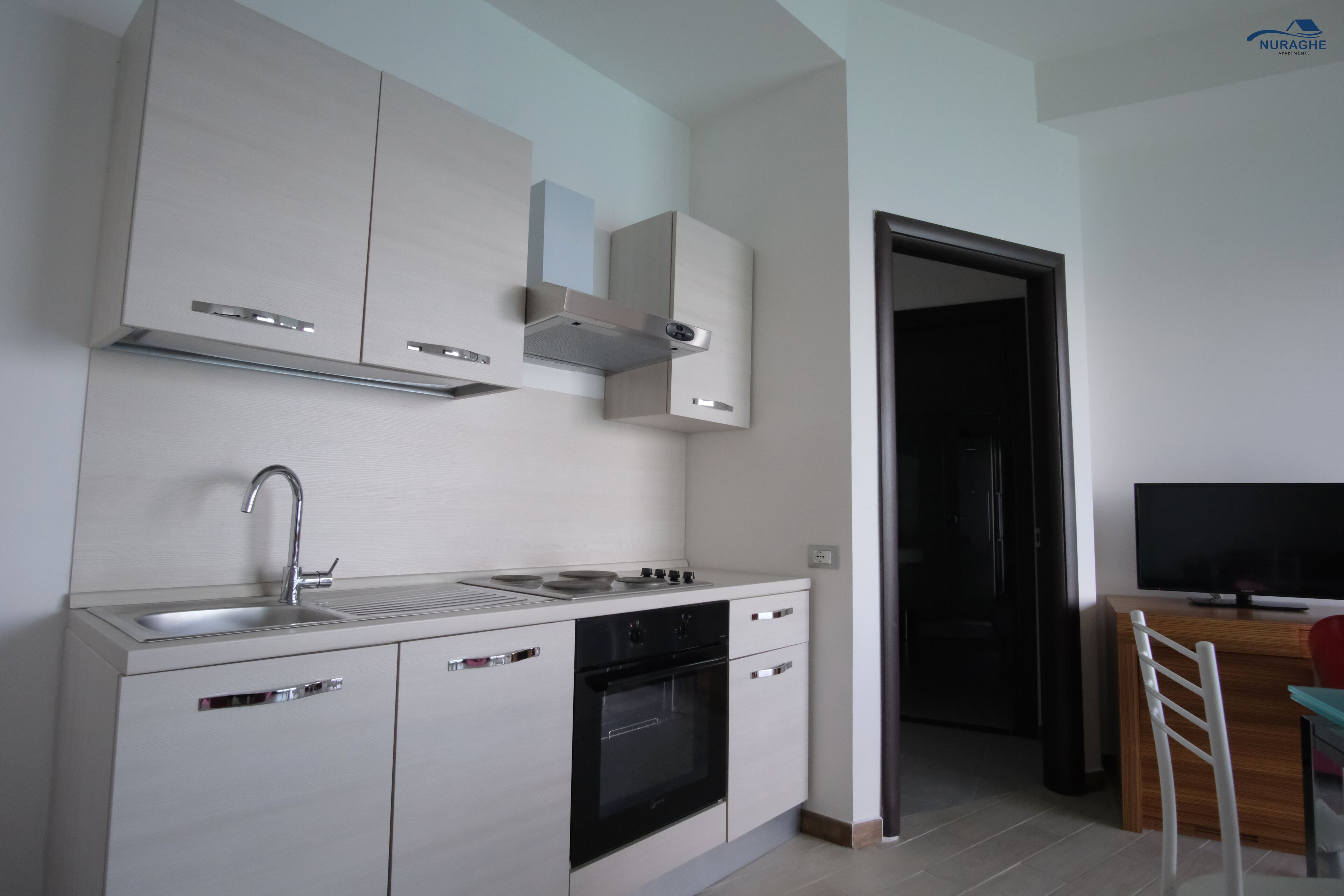 Uma cozinha moderna com forno embutido, pia de aço inoxidável e armários brancos.