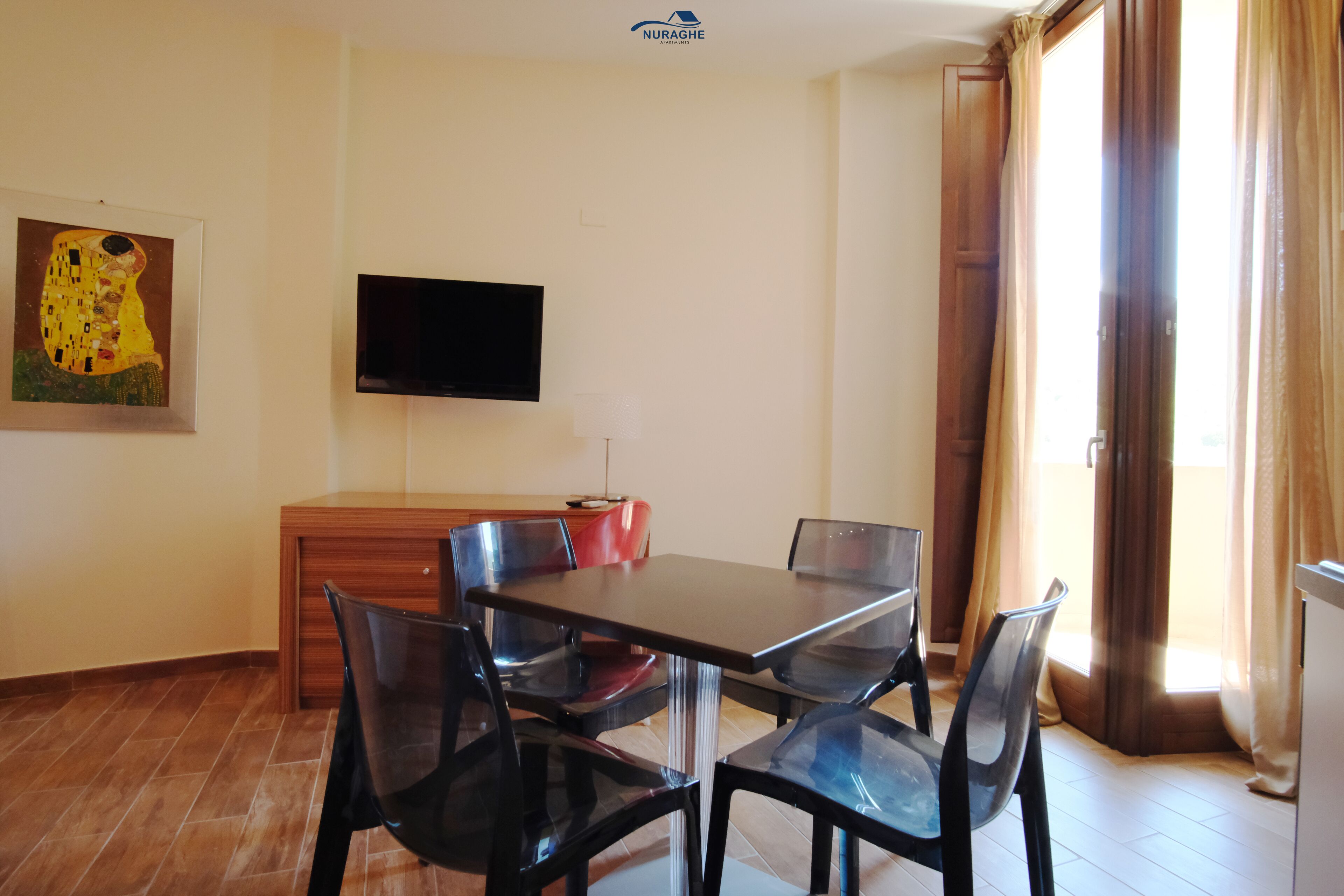 A dining area with a table and chairs, a flat-screen TV mounted on the wall, and a painting on the wall.
