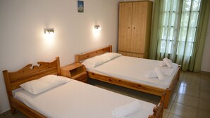 Zwei Holzbetten mit weißen Leinen und Handtüchern, ein Holzschrank und ein kleiner Nachttisch.