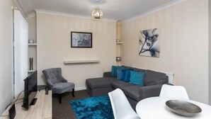 A modern living room with a grey sectional sofa, a white table, and a blue rug. - Cecil Lodge - 2 Bed Apartment (Swansea)