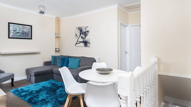 A modern living room with a grey sofa, white chairs, a round table, and a blue rug. - Cecil Lodge - 2 Bed Apartment (Swansea)