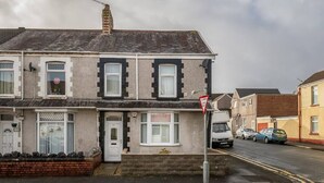 A two-story residential building with a white door, windows with white frames, and a brick facade. - Cecil Lodge - 2 Bed Apartment (Swansea)