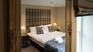 A bedroom with a large bed, two bedside tables with lamps, a plaid headboard, and a window with curtains.