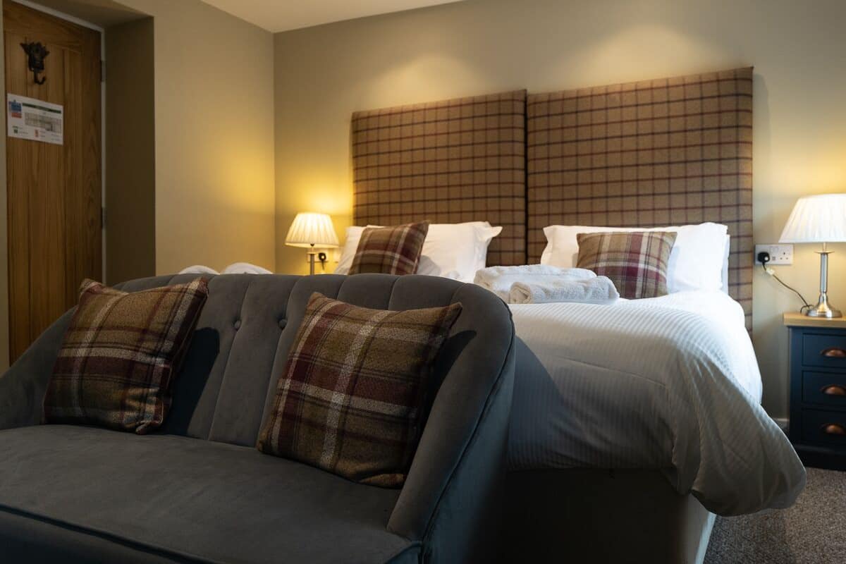 Habitación de hotel con sofá, dos camas y cabecero.