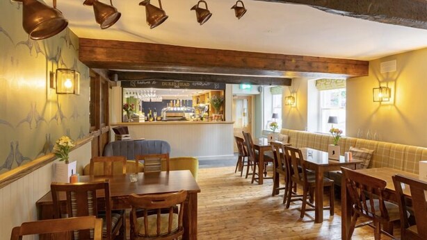 A restaurant interior with wooden tables and chairs, a bar area, and decorative wall sconces.