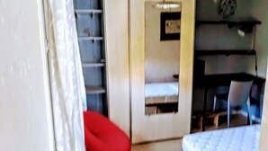 A room with a bed, a small table, and a chair. There is a window with a curtain partially drawn.