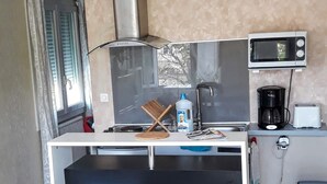 A compact kitchen with a microwave, toaster, and coffee maker. There are two stools in front of the counter.