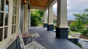 A covered outdoor patio with two white metal chairs and a small table, wooden ceiling, and large windows. - New Lower Rates! Amazing 8 Bedroom 3 Story Downtown Hot Springs! No Admin Fee!! (Hot Springs)