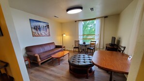 A living room with a brown leather sofa, a wooden coffee table, a round ottoman, a dining table with four chairs, and a painting on the wall. - New Lower Rates! Amazing 8 Bedroom 3 Story Downtown Hot Springs! No Admin Fee!! (Hot Springs)