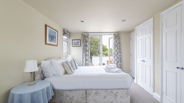 A neatly arranged bedroom with a bed, bedside tables, and a view of the outdoors through a large window. - JOIVY Charming 3 bed house with a rooftop terrace (London)