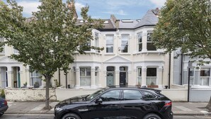 A black car parked in front of a white townhouse with a gabled roof and bay windows. - JOIVY Charming 3 bed house with a rooftop terrace (London)