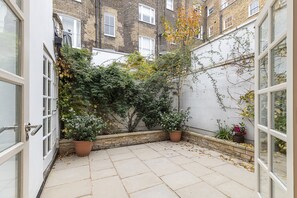 A courtyard with a tiled floor, potted plants, and a brick wall. - JOIVY Stunning 3BR house near Regents Park& Baker Street (London)