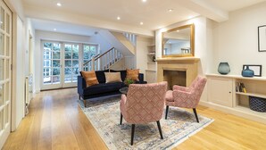 A spacious living room with a fireplace, a staircase, and a large window. - JOIVY Stunning 3BR house near Regents Park& Baker Street (London)
