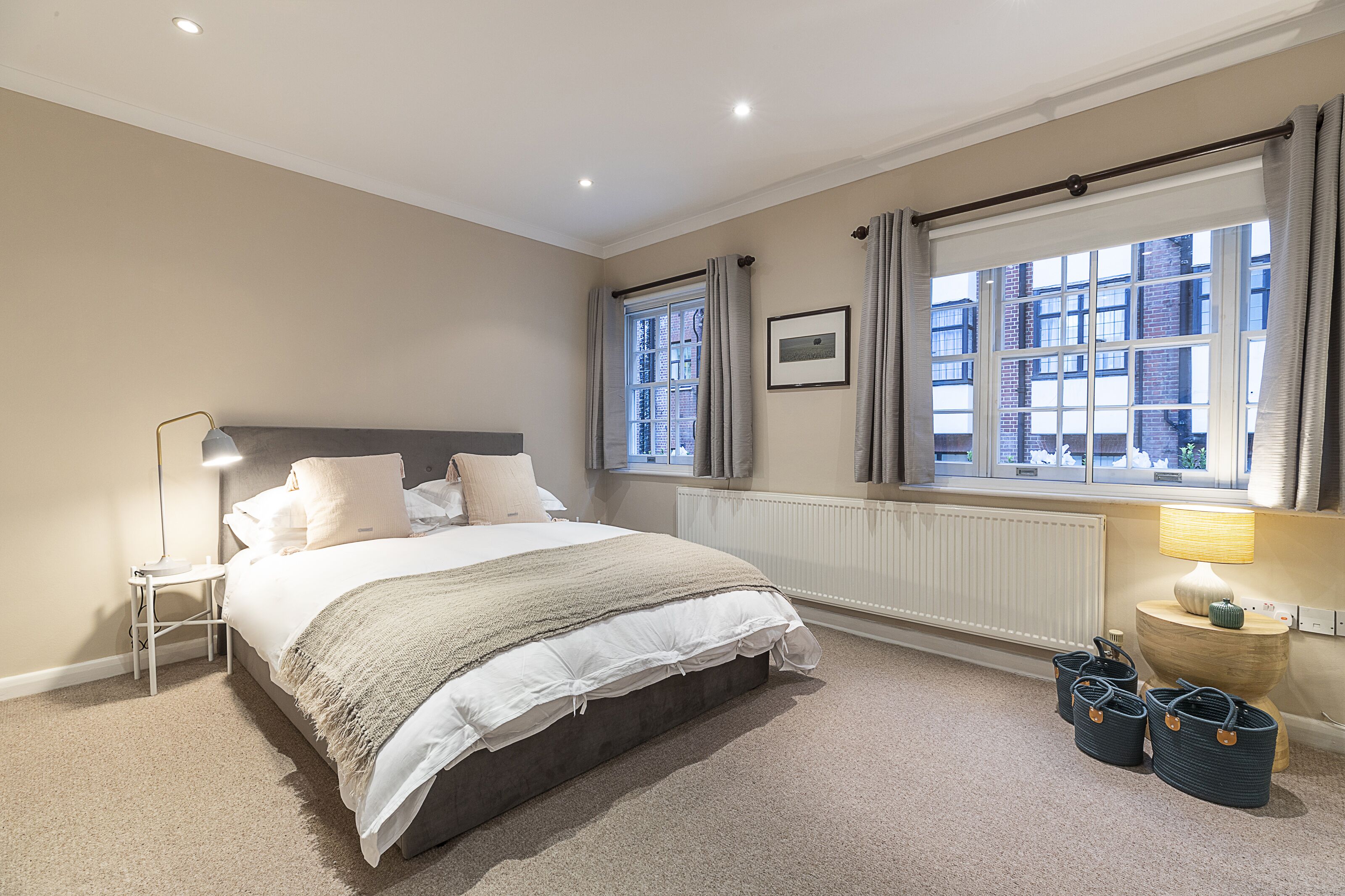 A bedroom with a bed, bedside lamp, window, radiator, and storage baskets.