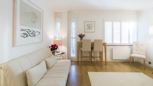 A spacious living room with a sofa, a dining area with chairs, a table, and a radiator. - JOIVY Sublime 1 bed flat with Thames view (London)