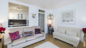 A living room with two sofas, a coffee table, a bookshelf, and a dining area with a kitchen visible through an open door. - JOIVY Sublime 1 bed flat with Thames view (London)