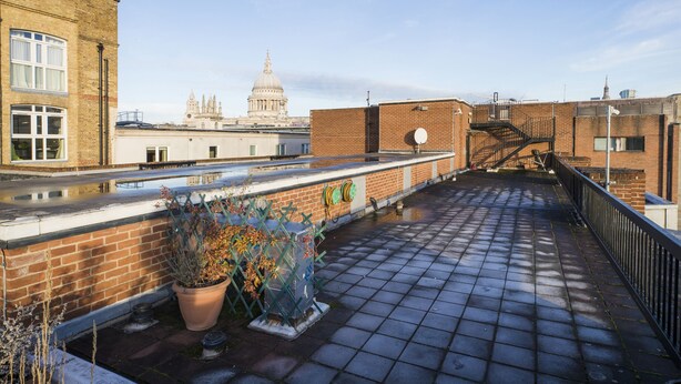 A rooftop terrace with a brick wall, a potted plant, and a view of a historic building in the background. - JOIVY Sublime 1 bed flat with Thames view (London)