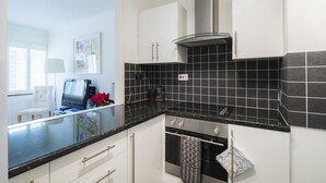 A modern kitchen with white cabinets, black tiles, a stainless steel range hood, and a glass backsplash. - JOIVY Sublime 1 bed flat with Thames view (London)