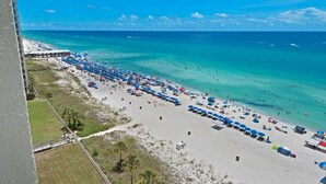 Ein Strand mit vielen Sonnenschirmen, Menschen, einer Mole und einem strahlend blauen Himmel.