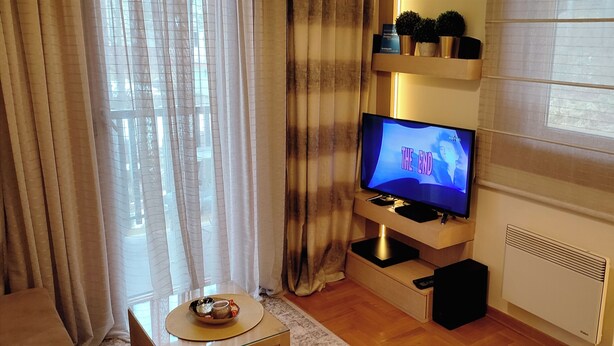 A living room with a flat-screen TV on a stand, a small table with a bowl and a cup, and a radiator on the wall. - Apartment Bubica Zlatibor Best for Family Holidays and Couples in Love (Zlatibor)