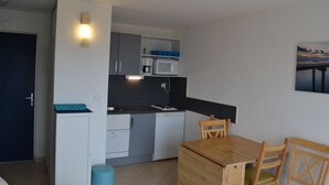 A compact kitchen with a microwave, coffee maker, and a sink. There is a dining table with chairs and a small stool. - Waterfront apartment (Lacanau Océan)