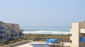 A beachfront view with a sandy area, a blue tarp, and buildings with balconies. - Waterfront apartment (Lacanau Océan)
