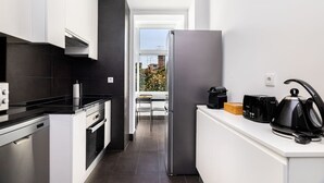 Una cocina moderna con armarios blancos, encimera negra, lavavajillas de acero inoxidable, horno integrado, refrigerador, cafetera y hervidor.