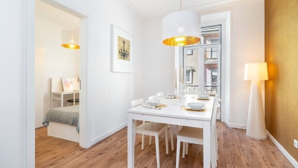 Un comedor con una mesa blanca dispuesta para cuatro personas, una lámpara colgante y una obra enmarcada en la pared.