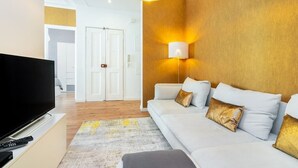 Una sala moderna con un televisor de pantalla plana, un sofá con cojines, un tapete estampado y una lámpara de pared.